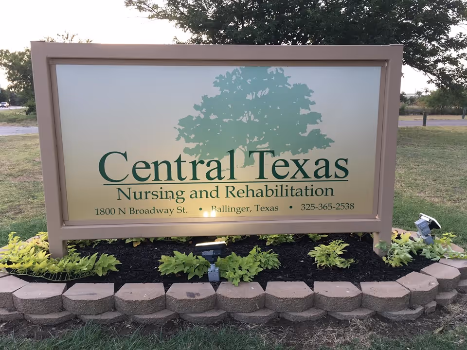 Outdoor sign for Central Texas Nursing and Rehabilitation located at 1800 N Broadway St., Ballinger, Texas, with a large tree graphic in the background and surrounded by small plants and a stone border.
