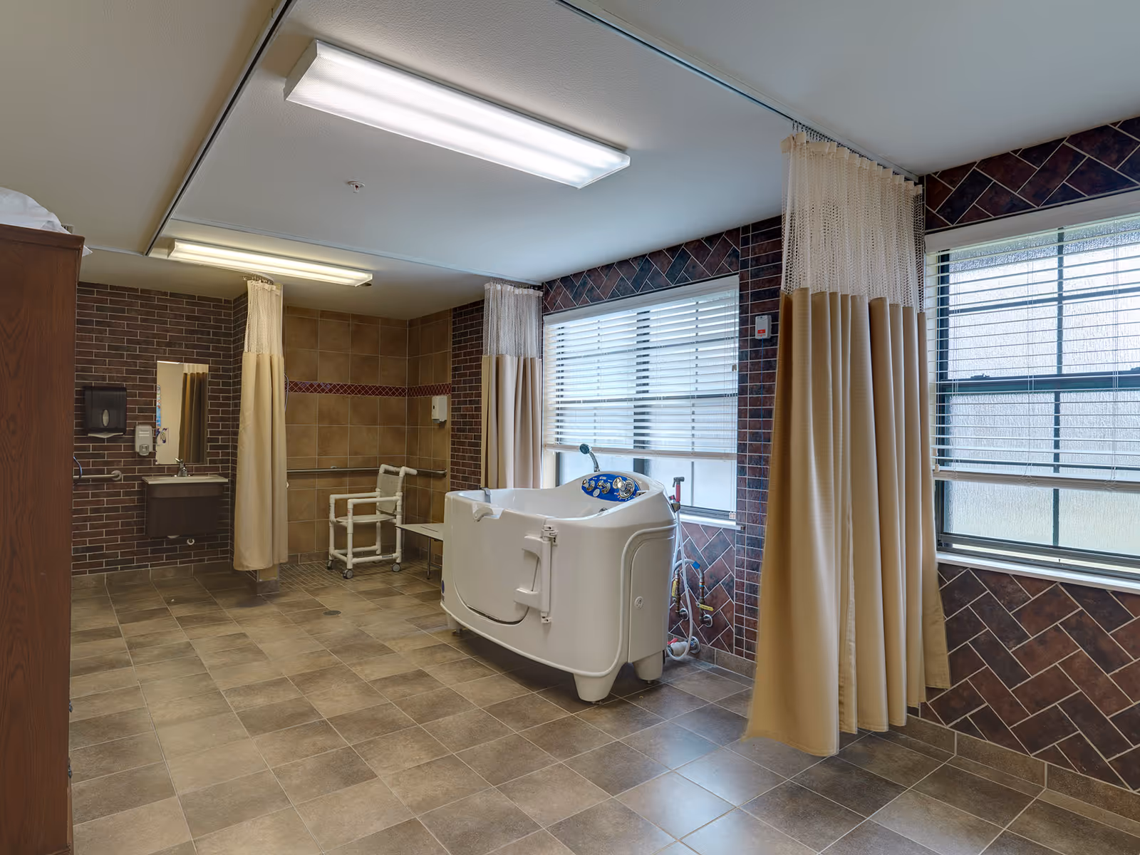 Assisted bathing room with a walk-in tub, shower chair, sink, privacy curtains and large windows.