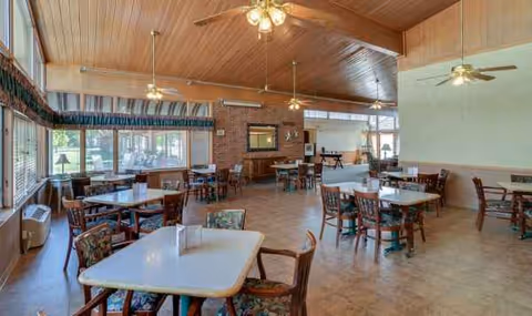 A spacious senior living dining room with multiple tables, chairs, and a brick fireplace.