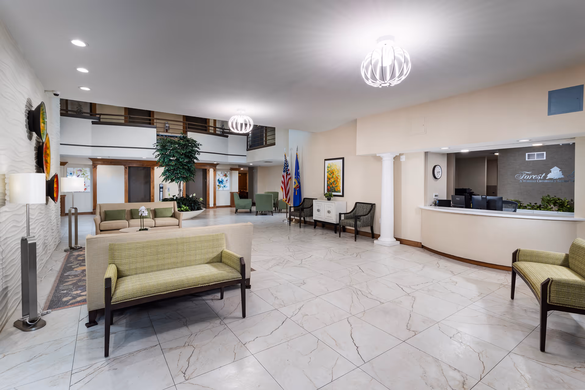 Spacious reception lobby with seating, a front desk, decorative lighting, and indoor plants.