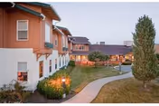 Curved walkway through a landscaped courtyard between two-story senior living buildings at dusk.