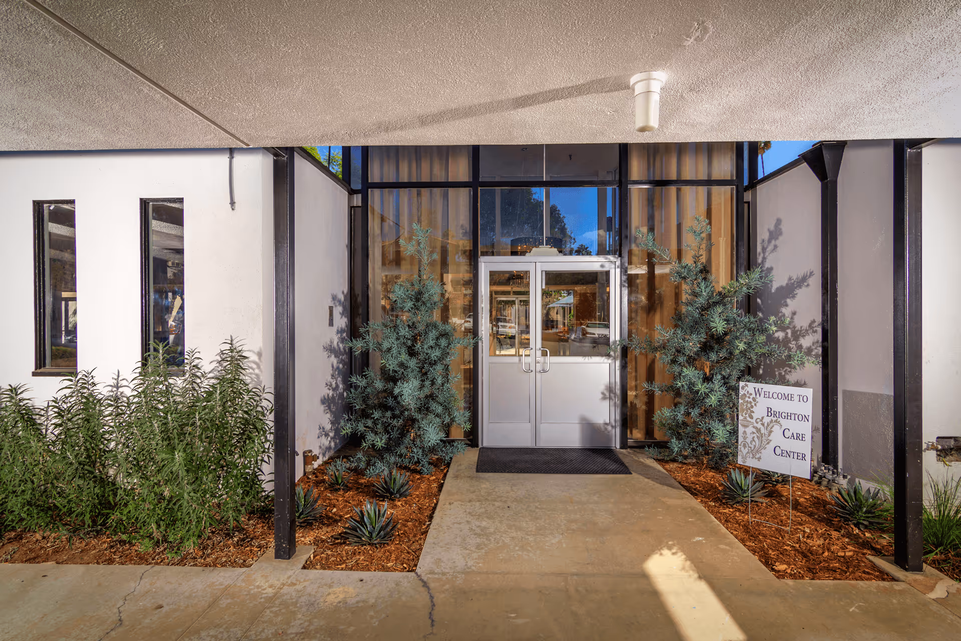 The Brighton Care Center entrance with double glass doors, plants on either side, and a welcome sign.