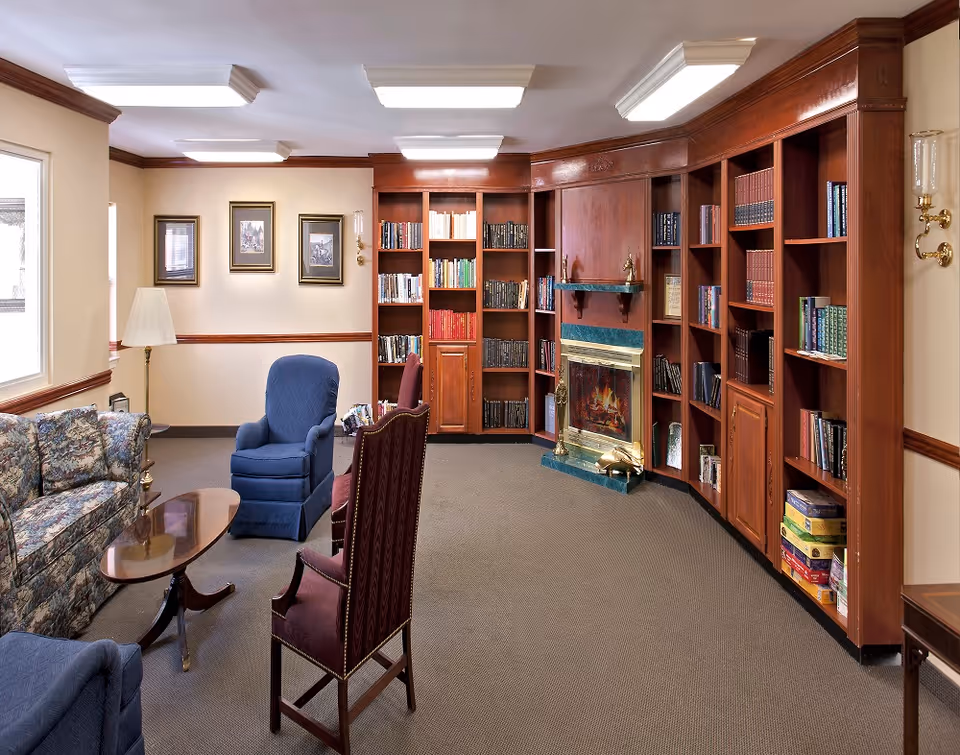 Cozy common room with upholstered chairs and sofa, a coffee table, built-in wooden bookshelves and a fireplace.