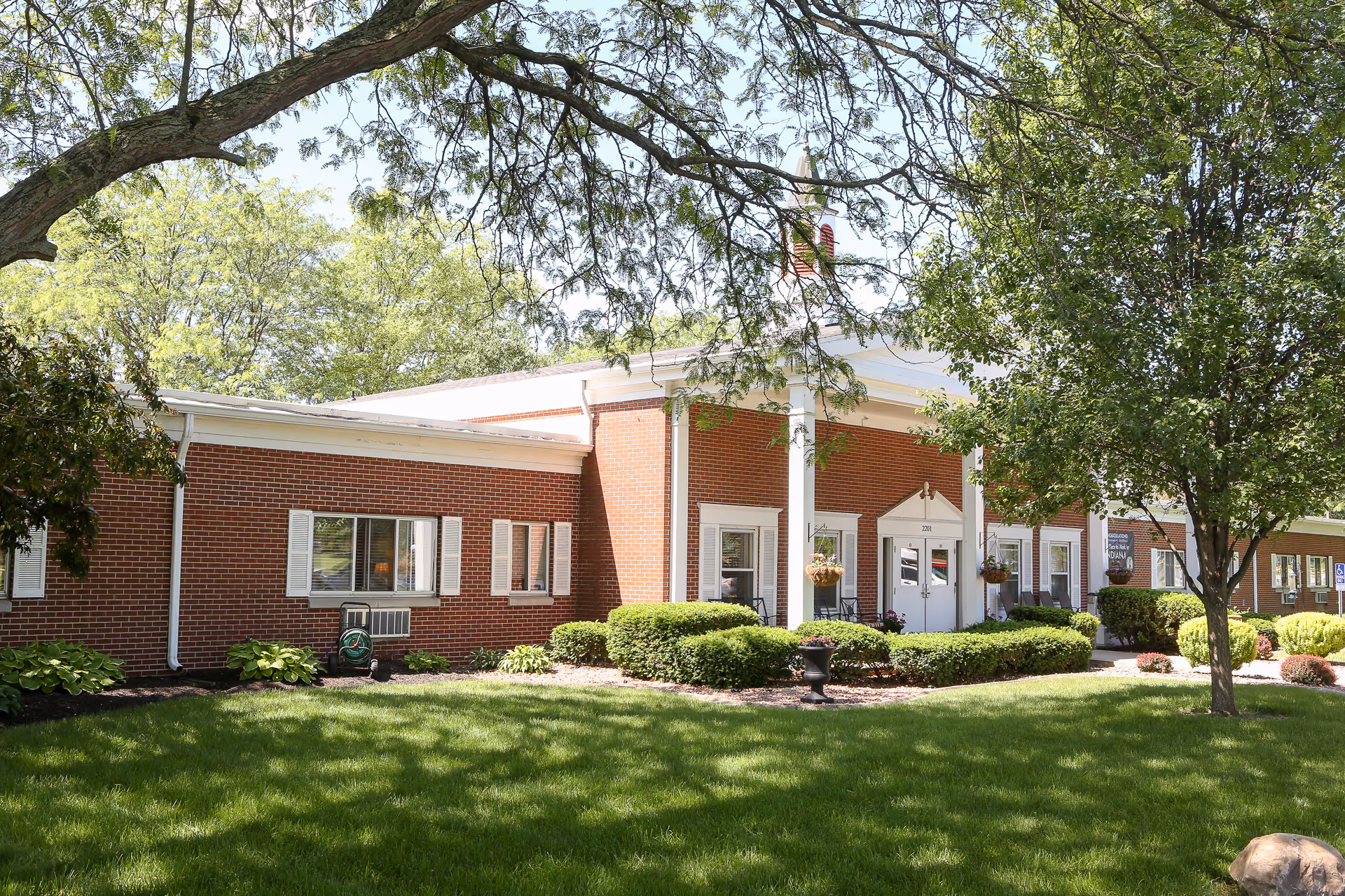 Front exterior of St. Mary Healthcare Center, a single-story red-brick building with white columns, landscaped lawn and trees.