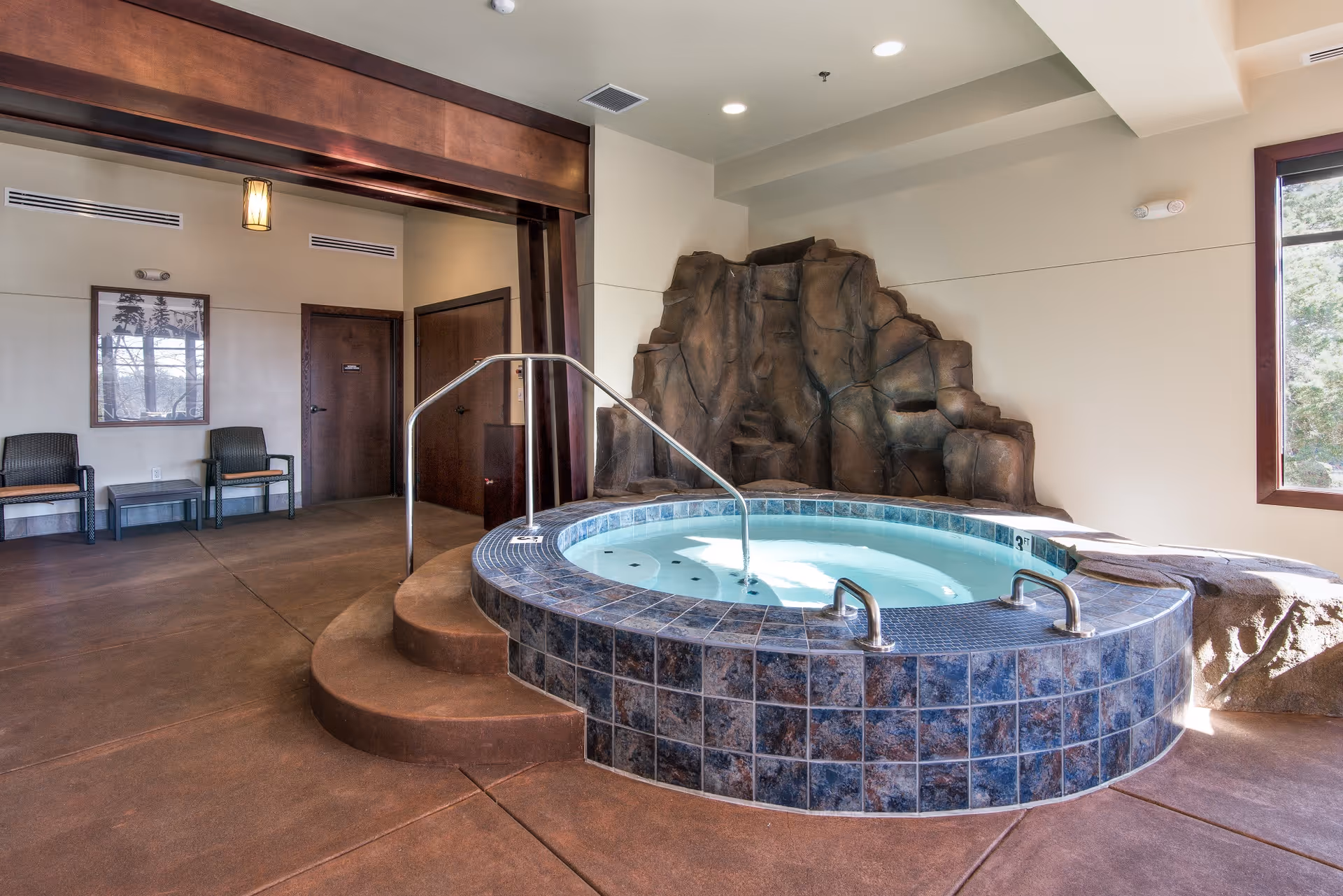 An indoor spa features a circular tiled hot tub, a rock feature, and seating area.