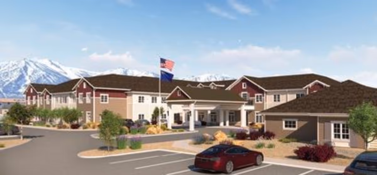 Exterior view of Valage Senior Living At Carson Valley facility with a two-story building, landscaped surroundings, parked cars, and mountains in the background under a clear sky.