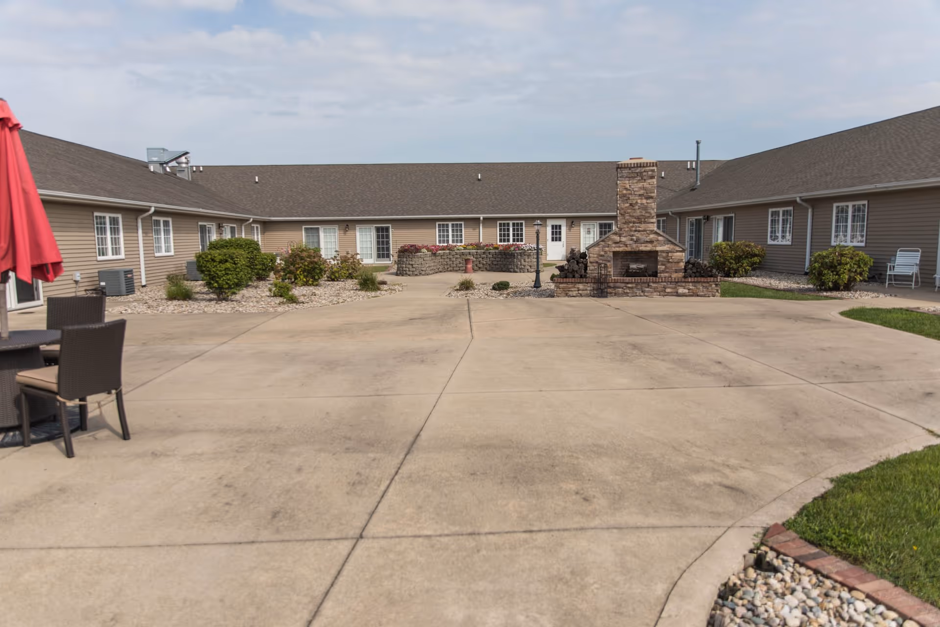 Open courtyard with a concrete patio, central stone fireplace, patio seating and a single-story building surrounding it.