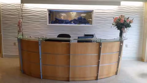 Curved wooden reception desk in a bright interior lobby with an in-wall aquarium.