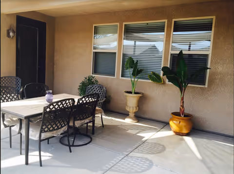 Outdoor patio with table, chairs, and potted plants by a beige wall.