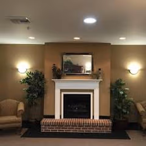 A warmly lit living room with a brick fireplace, mantle decor, and two armchairs.