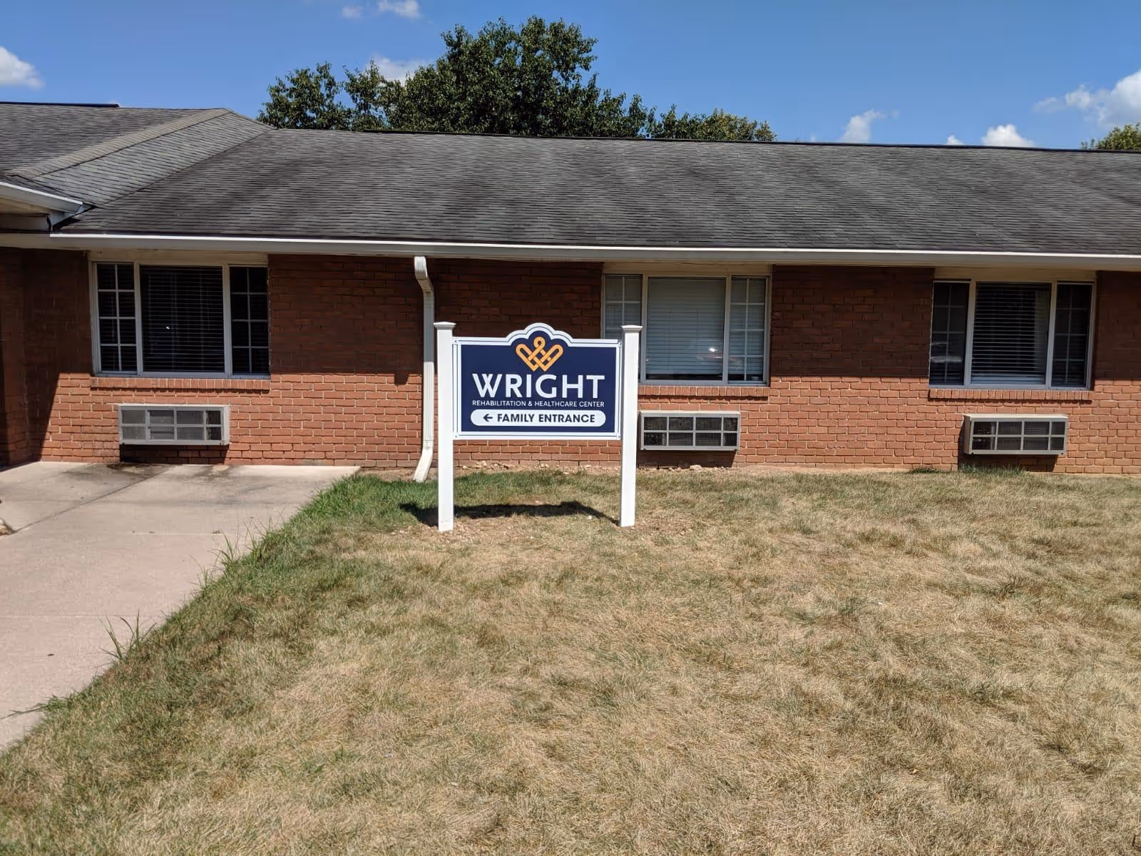 Brick front of Wright Rehabilitation & Healthcare Center with a freestanding sign on a grass lawn in front of windows.