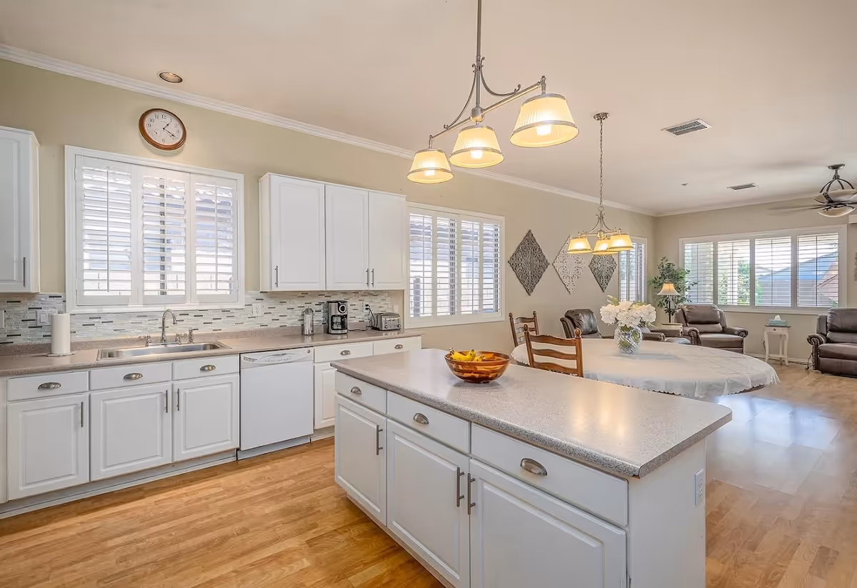 Bright open kitchen with white cabinets, a center island, and an adjacent dining and living area with large windows.