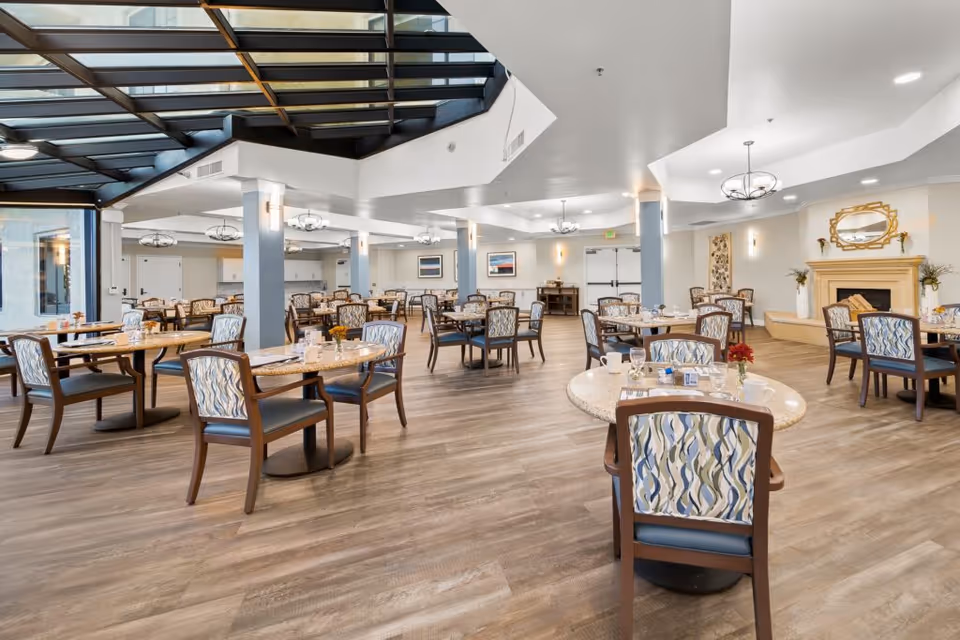 Bright, spacious dining room with round tables and patterned chairs beneath skylights and modern light fixtures.