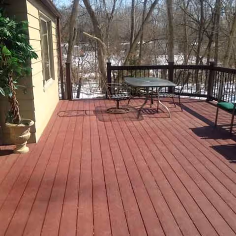 Outdoor wooden deck with a table, chairs, railing, and surrounding trees.