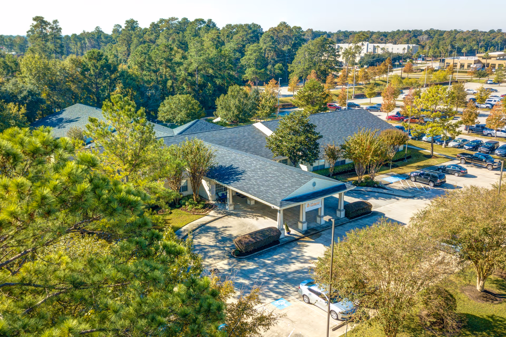 Aerial view of a senior living facility with an entrance canopy, surrounding trees, and parked cars in the parking lot.