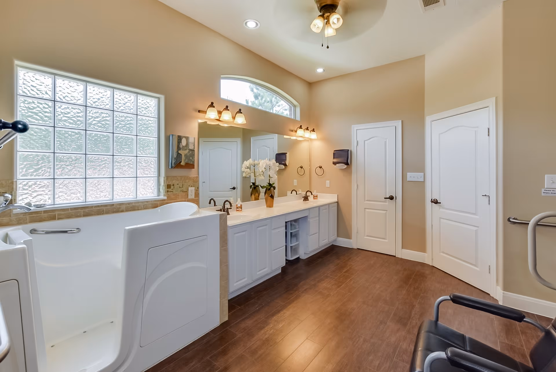 Spacious accessible bathroom featuring a walk-in tub, double sinks with large mirror, frosted glass window, and seating.