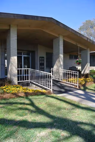 Front entrance of a senior care facility with a ramp, columns, and a hanging basket.