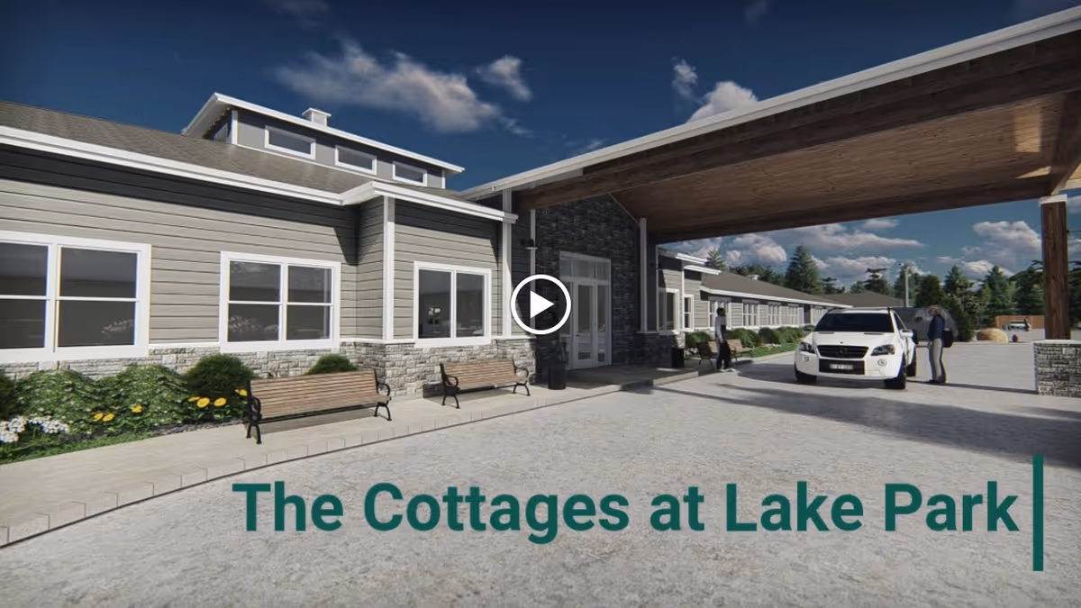 Front exterior of a single-story senior living facility with a covered entrance, benches, a parked car, and overlaid text reading 'The Cottages at Lake Park'.