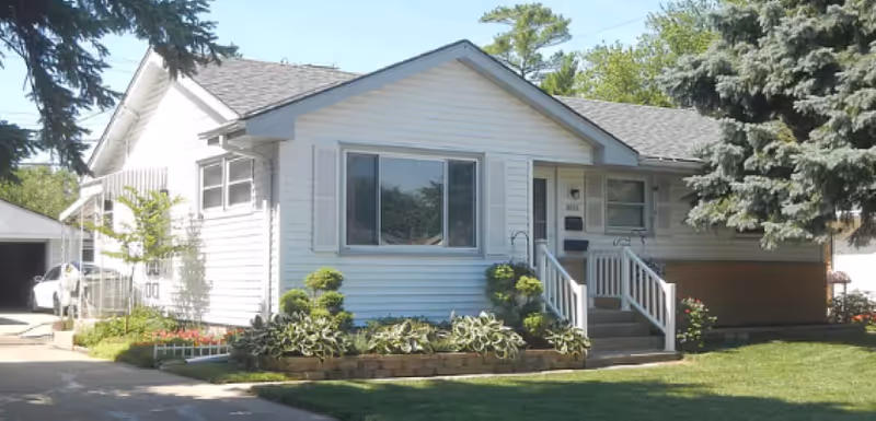 Front exterior of a white single-story house with steps and a landscaped yard.