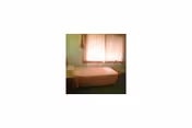 Small single-bed bedroom with a window covered by sheer curtains, a bedside table, and green carpet.