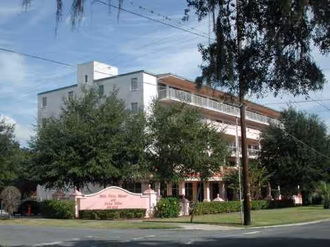 Exterior view of a multi-story senior living building with a pink front sign and lush trees.