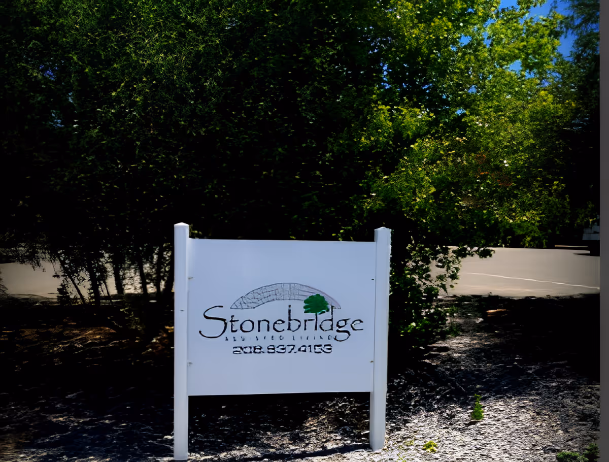 White Stonebridge sign posted in front of trees with a parking area visible behind it.