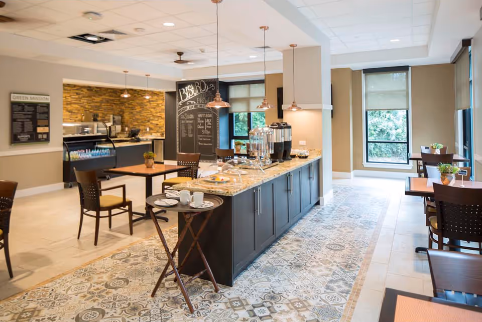 Bright bistro-style dining area with a central service island, tables and chairs, and large windows.