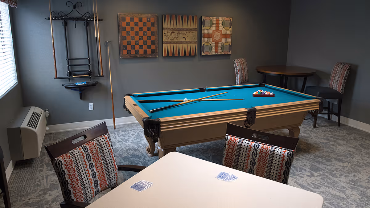 Game room with a teal-felt pool table, cue sticks, and seating including patterned chairs and a card table.