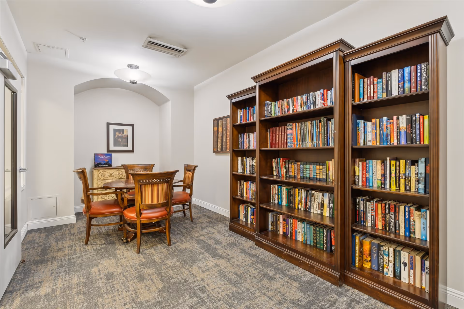 Small library/reading room with tall wooden bookshelves filled with books and a round table with four chairs.