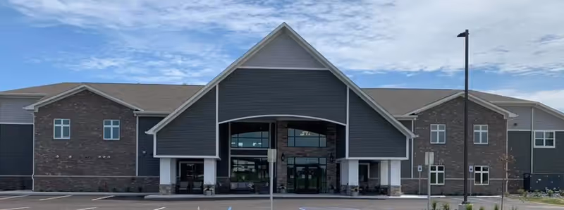 Front view of a modern senior living facility with a covered entrance and parking lot.