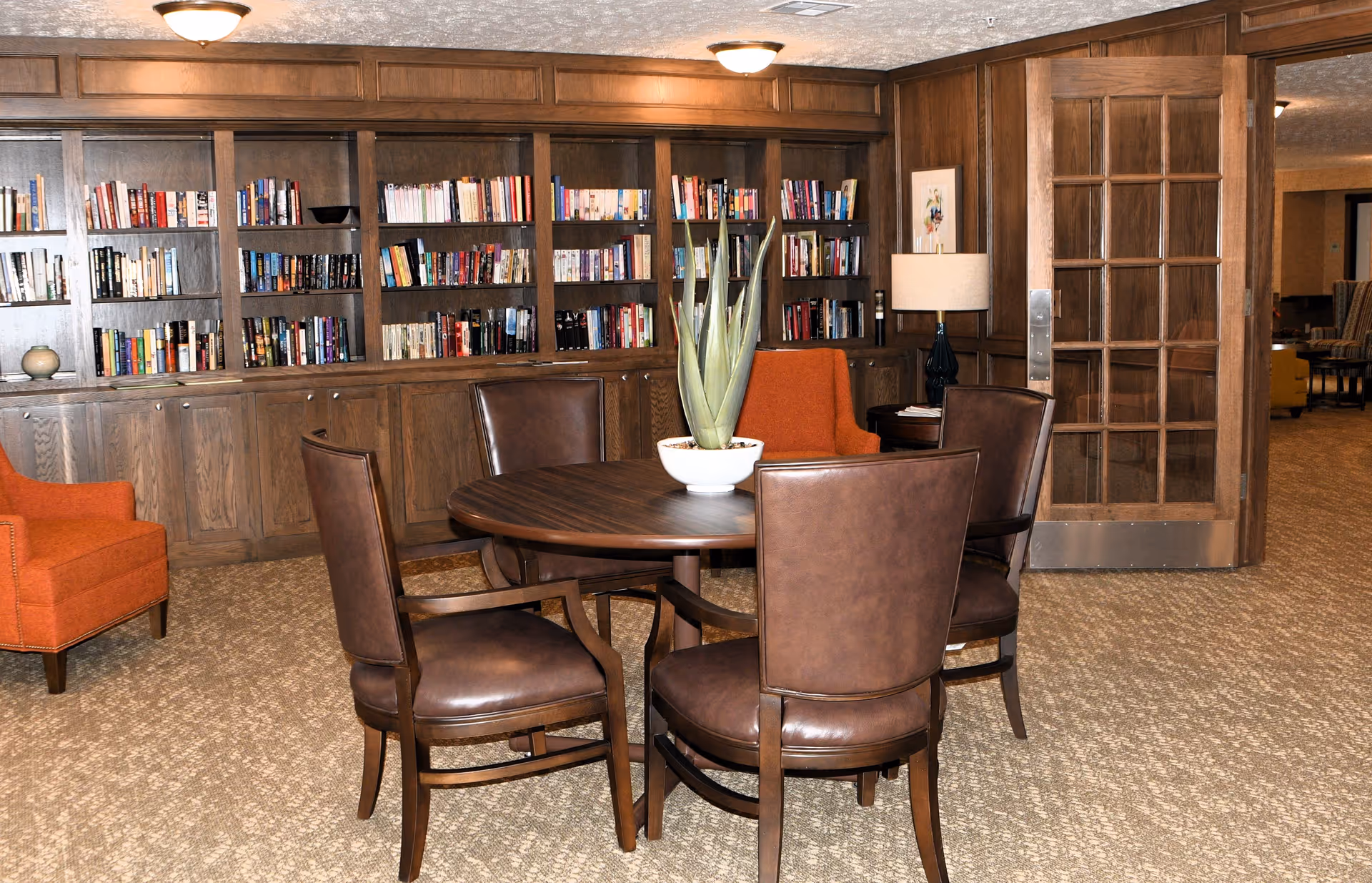 A communal lounge with a round wooden table and leather chairs in front of built-in wood bookshelves.