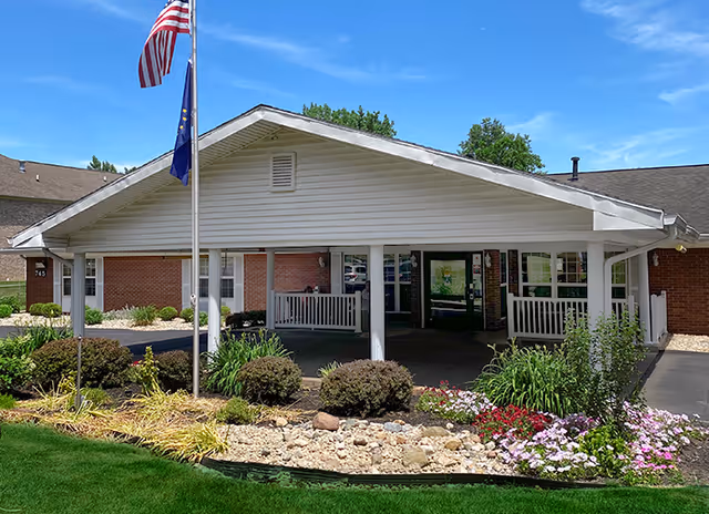 Single-story brick care center with a white covered entrance porch, flagpoles, and landscaped flower beds.