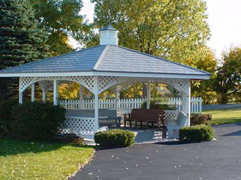 A white lattice gazebo with benches sits in a sunny outdoor area.