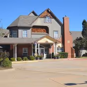 Two-story assisted living building with brick chimney and covered entrance, parking area in front.