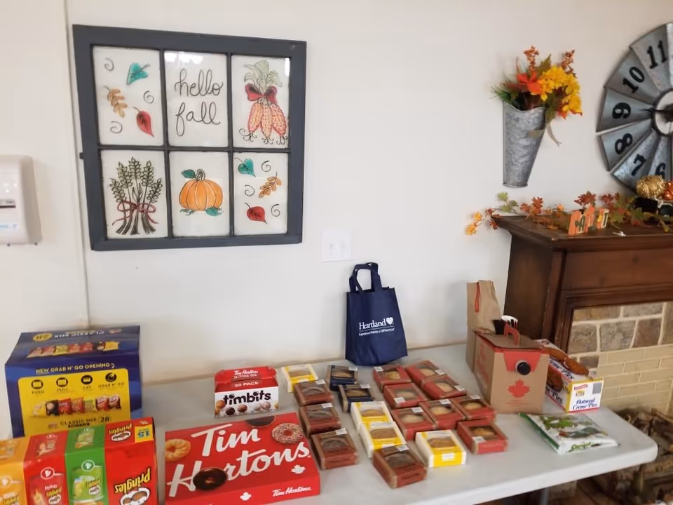 Table with assorted packaged snacks and Tim Hortons boxes set up against a decorated wall with fall-themed decor and a fireplace mantle.