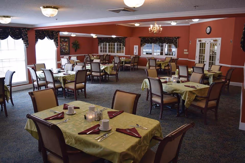 Spacious dining room with multiple tables set with green tablecloths, chairs, and place settings.