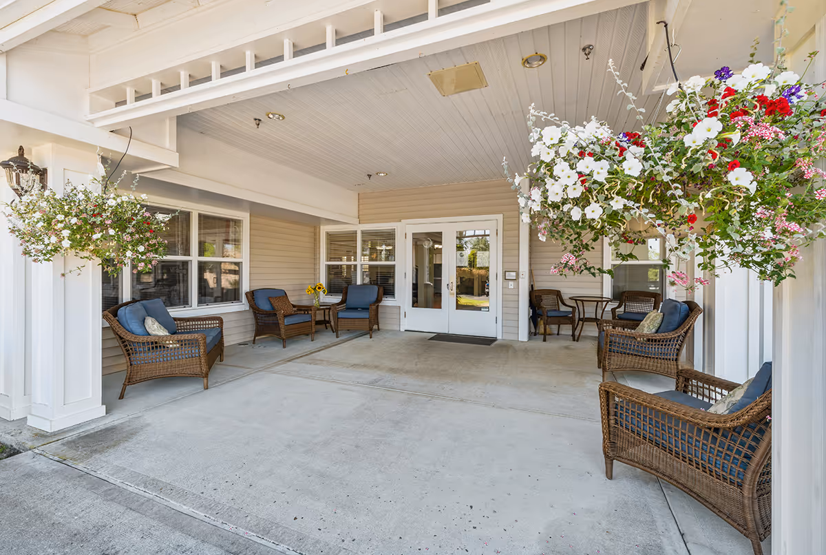 Covered entrance patio with wicker chairs, tables, and hanging flower baskets in front of double doors.