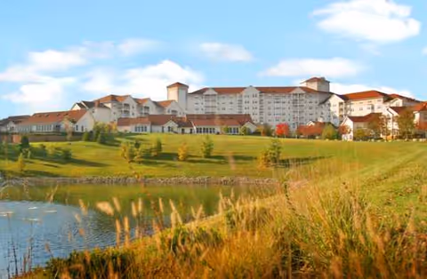 A large multi-wing senior living facility sits on a grassy hill by a pond.