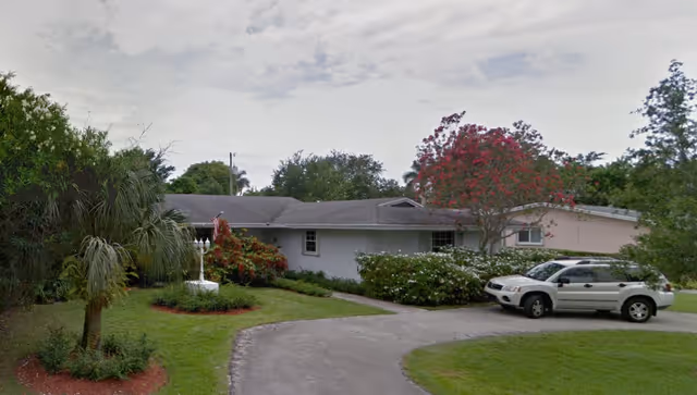 Exterior view of Sun Bay Manor with a circular driveway and parked SUV.