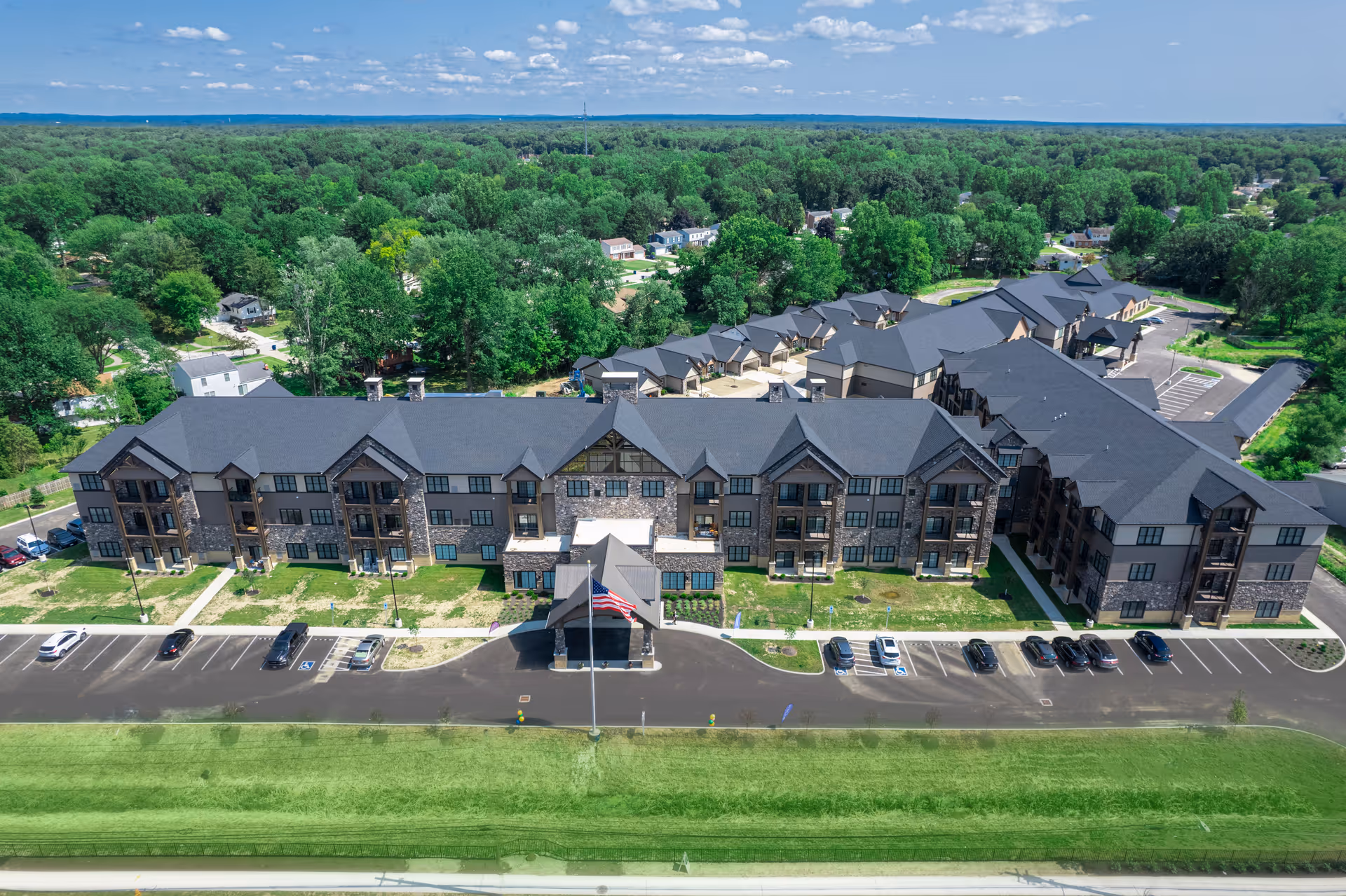 Aerial view of a three-story senior living community building with parking lot and surrounding trees.