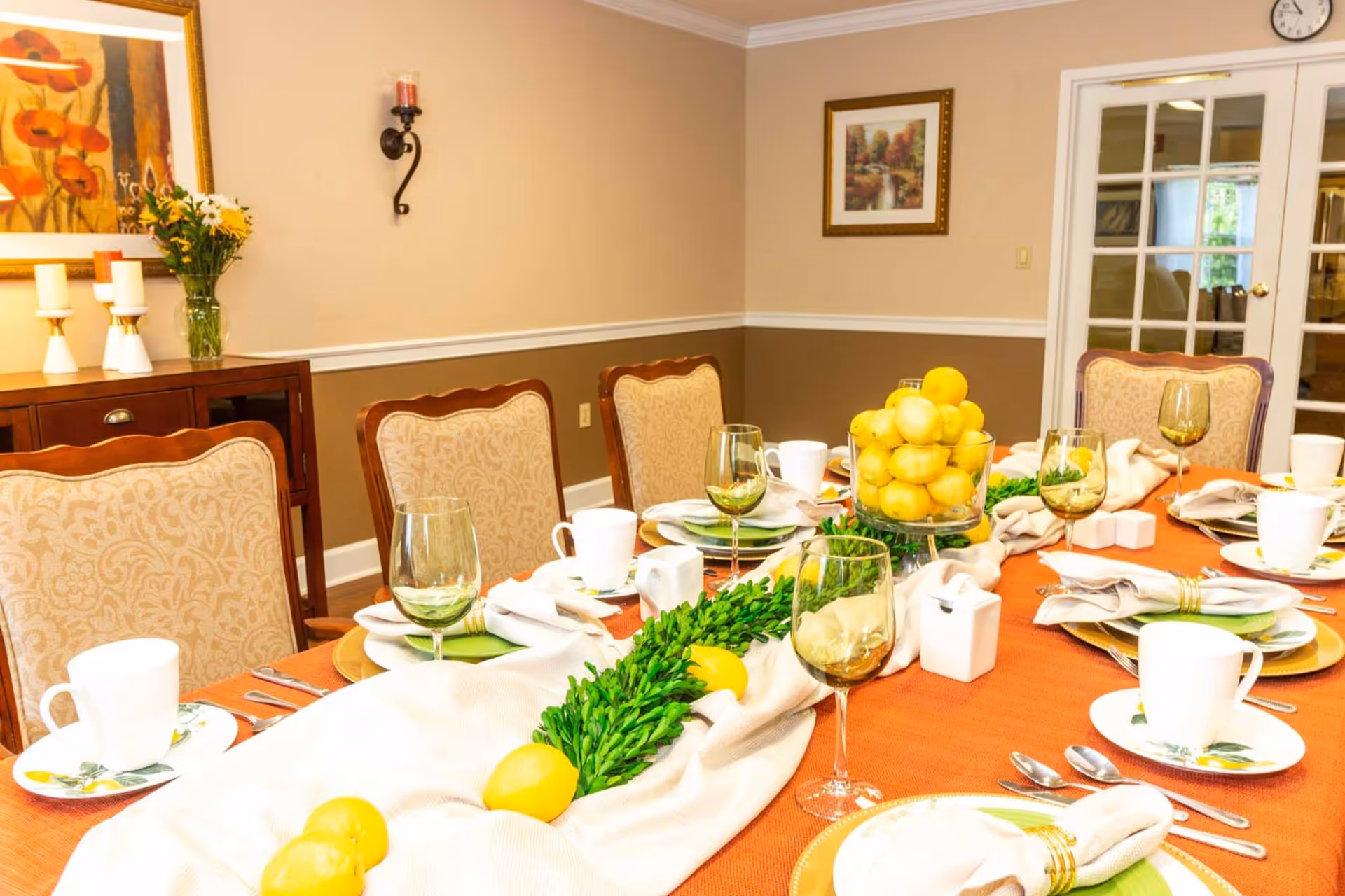 A formally set dining table with place settings, wine glasses, decorative lemons and greenery in a cozy dining room.