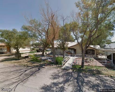 Exterior view of Lucero Residential Care Facility with trees, walkway, and fenced outdoor seating area.