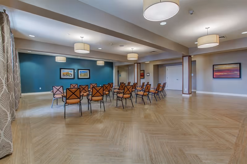 Spacious multipurpose common room with rows of chairs, a teal accent wall, pendant lights, and wood-patterned flooring.