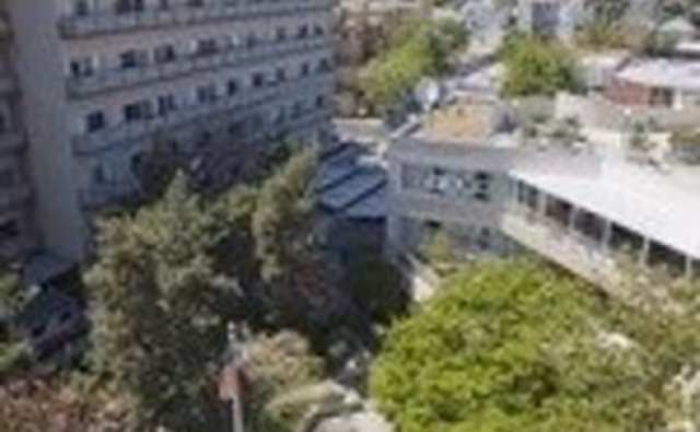 Aerial view of a multi-story building complex surrounded by trees and greenery, showing part of the facility's outdoor garden and courtyard area.