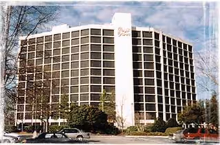 Tall senior living building with many windows and a parking lot.