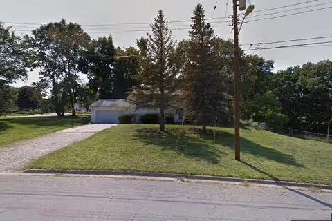 Front exterior of a single-story building with a grassy yard, driveway, and trees.