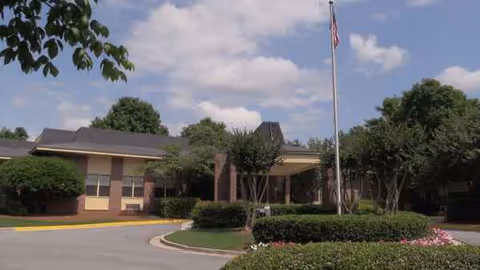 Exterior view of a single-story senior living facility with a flagpole and manicured landscaping.