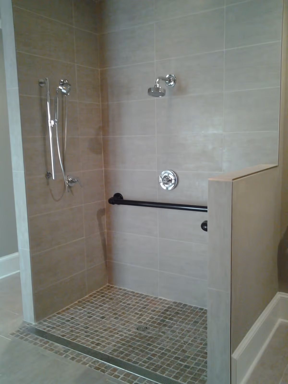 Tiled walk-in shower with an overhead and handheld shower, a horizontal grab bar, and a half wall.