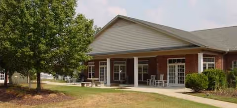 Front exterior of a brick senior living facility with a covered entry and rocking chairs.