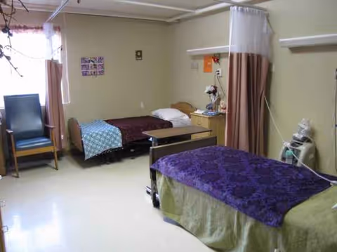 Shared patient room with two beds, curtains, and medical equipment in a nursing facility.